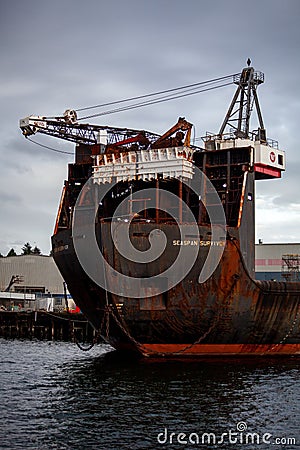 A large container ship is docked at Seaspan, named `Seaspan Survivor`. Cranes are atop this old, rusty ship and large anchor chai Editorial Stock Photo