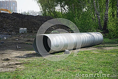 A large corrugated metal pipe with a coupler, prepared for installation, lies on a construction site next to a pile of gravel. Stock Photo