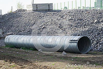 Large corrugated pipe with a coupler, prepared for installation, lies on a construction site next to a pile of gravel. Production Stock Photo