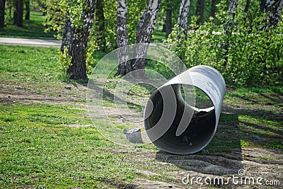 A large corrugated pipe, prepared for installation, lies on the ground in a park or square. Production of storm collector sewers. Stock Photo