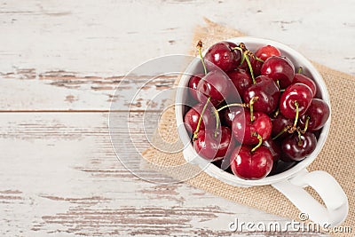 A large cup of coffee in front angel, white bowl full with fresh cherries, fruits. Light rustic background, shabby chic, vintage Stock Photo