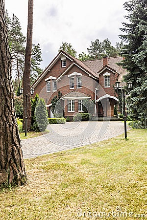 Large detached house exterior with brick walls and red roof behind a cobblestone path and green lawn in the summer Stock Photo