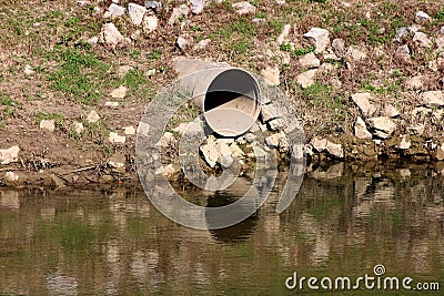 Large diameter storm drain concrete pipe exit surrounded with dirt covered large rocks and grass on side of river bank Stock Photo