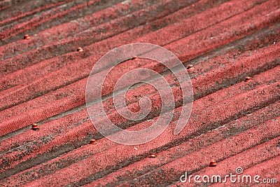 Large dilapidated dark red roof tiles with faded color texture background held together with strong red rivets Stock Photo