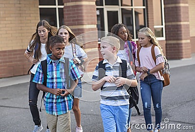 Large, diverse group of kids leaving school at the end of the day. School friends walking together and talking together on their w Stock Photo