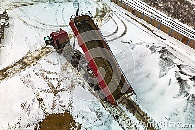 A large dump truck unloads rubble or gravel at a construction site in winter. Car tonar for transportation of heavy bulk cargo. Editorial Stock Photo