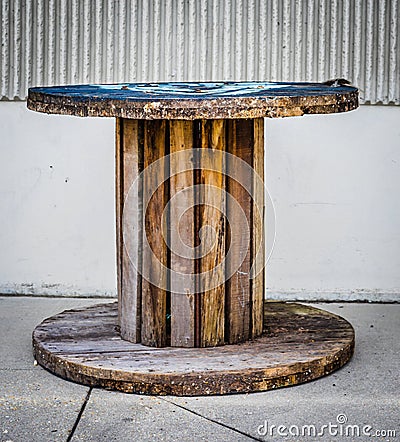 Large Empty Wooden Spool on sidewalk, and a white stripped pattern wall in the background. Stock Photo