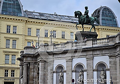 Large equestrian statue in Vienna. In the foreground the facade of a bridge with three statues and in the background a historic bu Editorial Stock Photo