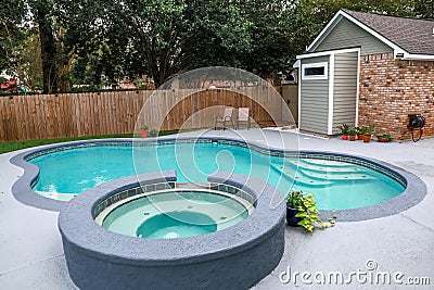 A large free form gray grey accent swimming pool with turquoise blue water in a fenced in backyard in a suburb Stock Photo