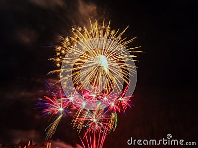 Large golden flash of fireworks and many small flashes in red with lilac sparks against a dark sky Stock Photo