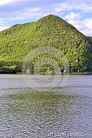 Large green hill casting reflectons onto Bonne Bay at Norris Point Stock Photo