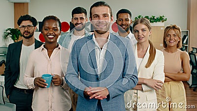 A large group of intelligent looking people are standing on their feet in an office crossing their arms and smiling Stock Photo