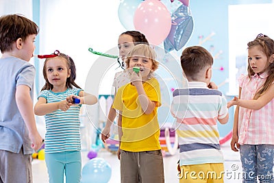 Large group of kids age 3 to 5 inside on a birthday party blowing noisemakers horns and twisted whistles Stock Photo