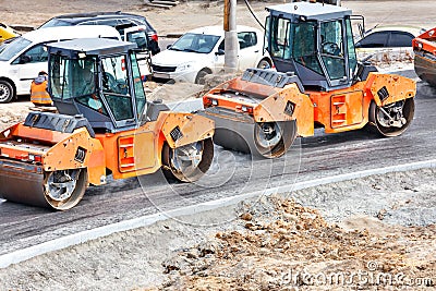 Large and heavy orange vibratory rollers compact the hot asphalt on the new road Stock Photo