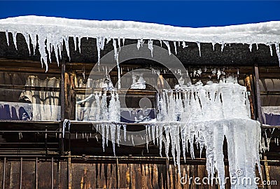 Large icicles hang from a house roof. Dangerous large icicles Stock Photo