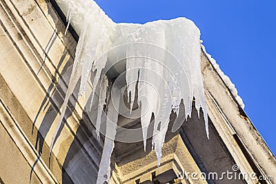 Large icicles hang from a house roof in winter. Dangerous large icicles. Death or injury danger. Stock Photo