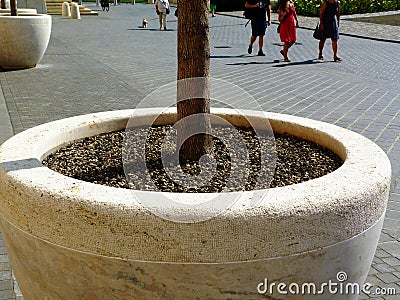 Grey precast concrete tree planter in urban setting. grey cobblestone pavement. people walking by Stock Photo