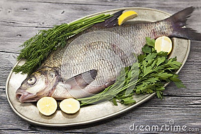 A large live bream river fish fish lying on a on on an iron tray with a knife and slices of lemon and with salt dill Stock Photo