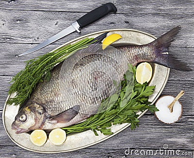 A large live bream river fish fish lying on a on on an iron tray with a knife and slices of lemon and with salt dill Stock Photo