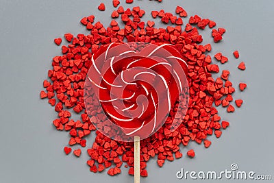 Large Lollipop on a stick in the shape of a heart surrounded by small hearts on a gray background Stock Photo