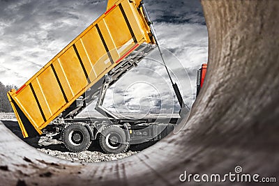 A large mining truck unloads the earth. A soil transporter with a raised body dumps soil. Contrast image against the sunset sky. Stock Photo