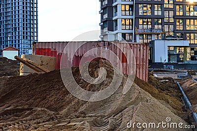 A large mountain of sand lies on a construction site in the city center. sand lies against the backdrop of large orange dumpsters Stock Photo