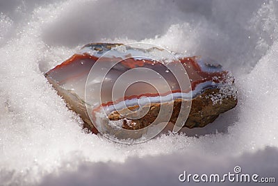 Large multi-colored layered piece agate chalcedony gem in the sunlight on the snow winter background close-up Stock Photo