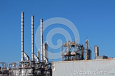 Large oil refinery industrial complex with three brand new shiny metal industrial chimneys and old long shipping container Stock Photo