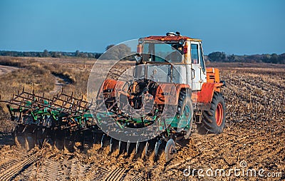 Large, old, beautiful tractor plowing the earth on the field after harvest autumn harvest sunflowers. Stock Photo