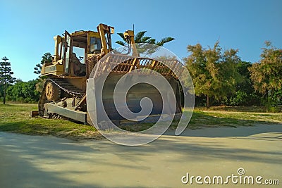 A large old bulldozer stands in a city park with a shovel lowered to the ground, defocused. Preparation for razing to Editorial Stock Photo