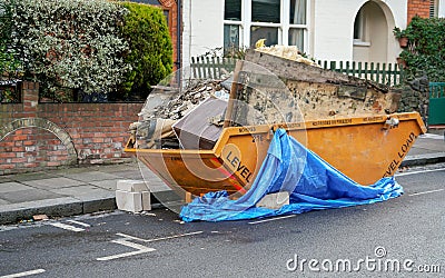 Large orange metal skip container in front house, full of rubbish from household reconstruction Stock Photo