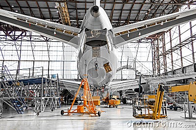 Large passenger aircraft on service in an aviation hangar rear view of the tail, on the auxiliary power unit. Stock Photo