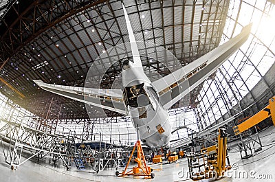 Large passenger aircraft on service in an aviation hangar rear view of the tail, on the auxiliary power unitand tail altitude cont Stock Photo