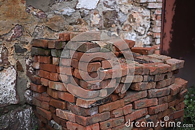 a large pile of red-orange bricks against the background of a broken old wall on the street. for introductory instructions books Stock Photo