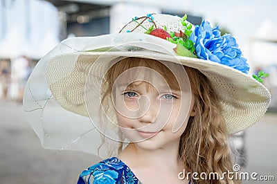 Large portrait of a lovely blue-eyed teenage girl in a straw hat with flowers. A charming girl with long fluffy hair looks at the Stock Photo