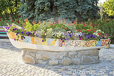 A large pot of flowers on the street. Street flowers in a pot of stone in the shape of a boat Stock Photo