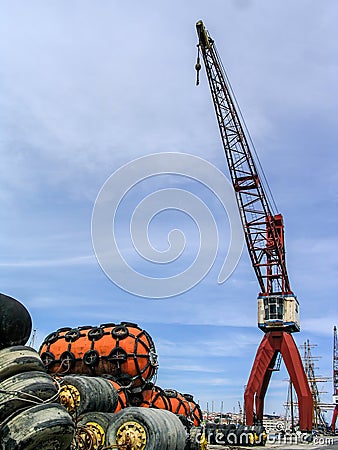 Large powerful Crane of a Harbor or Port and different types of ship fenders or ship tire bumpers to be used on moored ships. Stock Photo