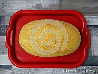 Large, ripe, yellow melon on a red tray. Appetizing oval melon. Photo in close-up Stock Photo