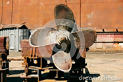 Large, rusted ship propeller displayed on wooden blocks in a shipping yard, symbolizing industrial maritime decommission Stock Photo