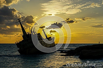 A large rusty shipwreck silhouette on a rocky coast against a beautiful sunset background Stock Photo