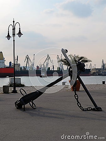 A large sea anchor adorns the walking part of the port, in the background are the water area of the port, cargo ships and cra Stock Photo