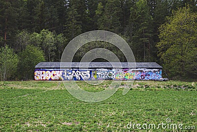 A large storage facility covered in graffiti. Large field with greenery and forest. Editorial Stock Photo