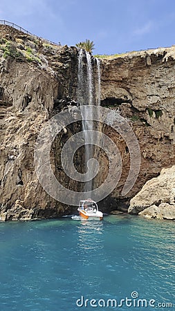 A large strong waterfall falls from a rocky precipitous shore into the blue Mediterranean Sea Stock Photo