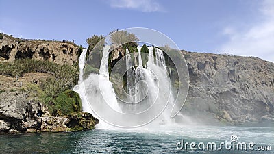 A large strong waterfall falls from a rocky precipitous shore into the blue Mediterranean Sea Stock Photo