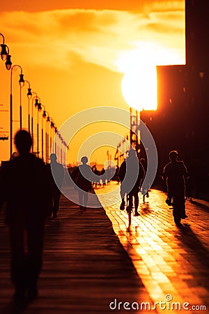 Large sun setting looking straight down a long boardwalk, with silhouettes of walkers and cyclists. Long Beach New York. Editorial Stock Photo