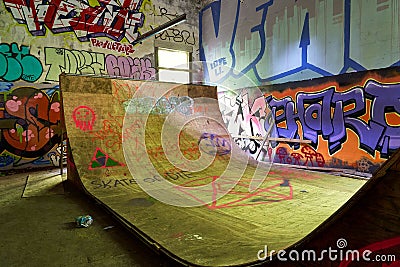 A large sunlit plywood skateboard ramp surrounded by walls covered in bright graffiti. Editorial Stock Photo