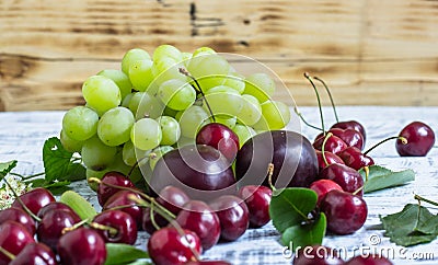 Large sweet juicy cherries, plums and grapes, foliage and flowers on a wooden background Stock Photo