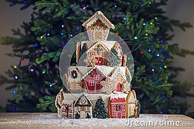 Large tiered Christmas cake decorated with gingerbread cookies and a house on top. Tree and garlands in the background. Stock Photo