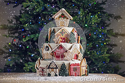 Large tiered Christmas cake decorated with gingerbread cookies and a house on top. Tree and garlands in the background. Stock Photo