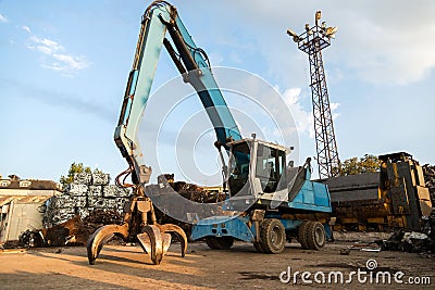 Large tracked excavator working a steel pile at a metal recycle yard. Industrial scrap metal recycling Stock Photo